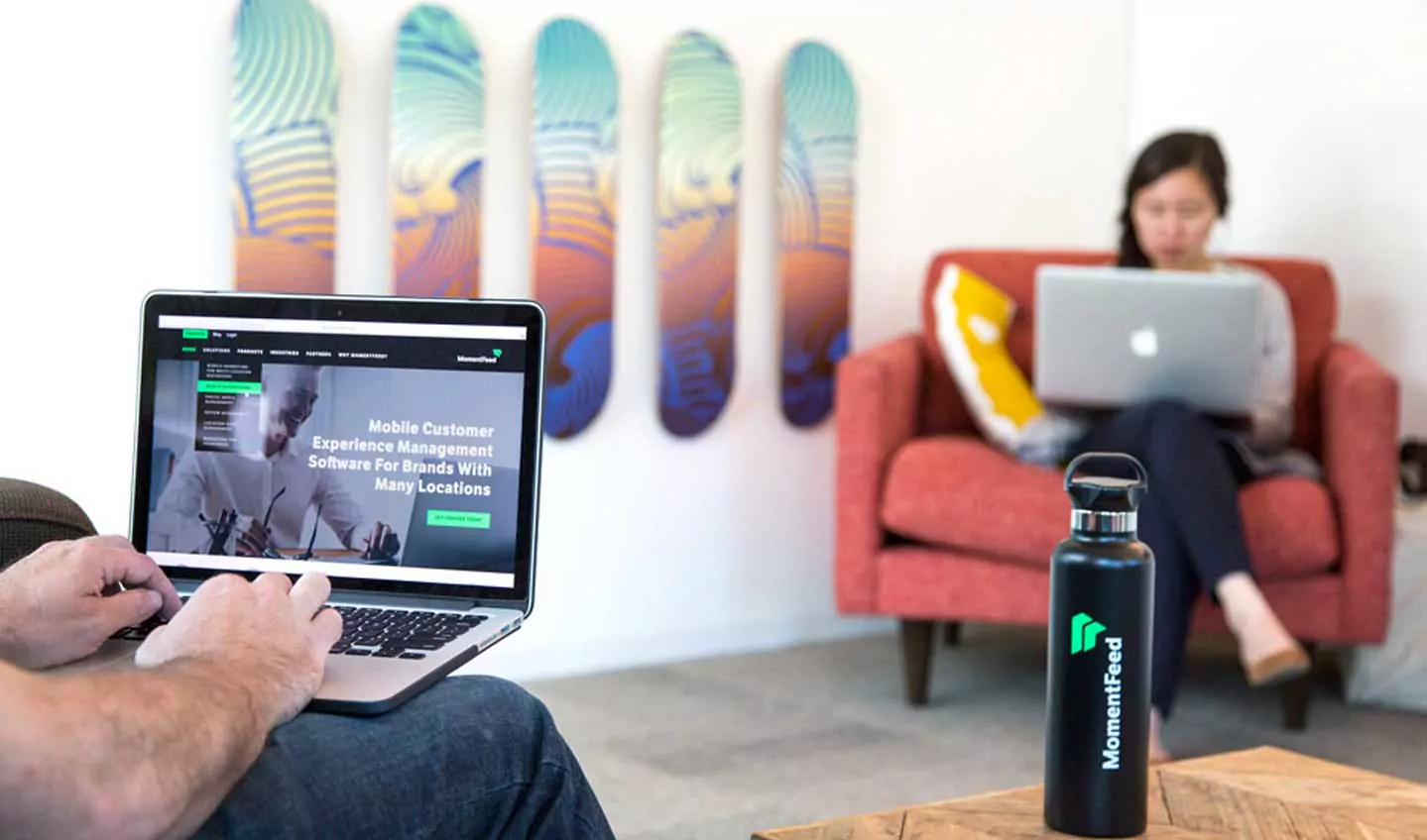 MomentFeed website on a laptop beside a branded water bottle in the MomentFeed office